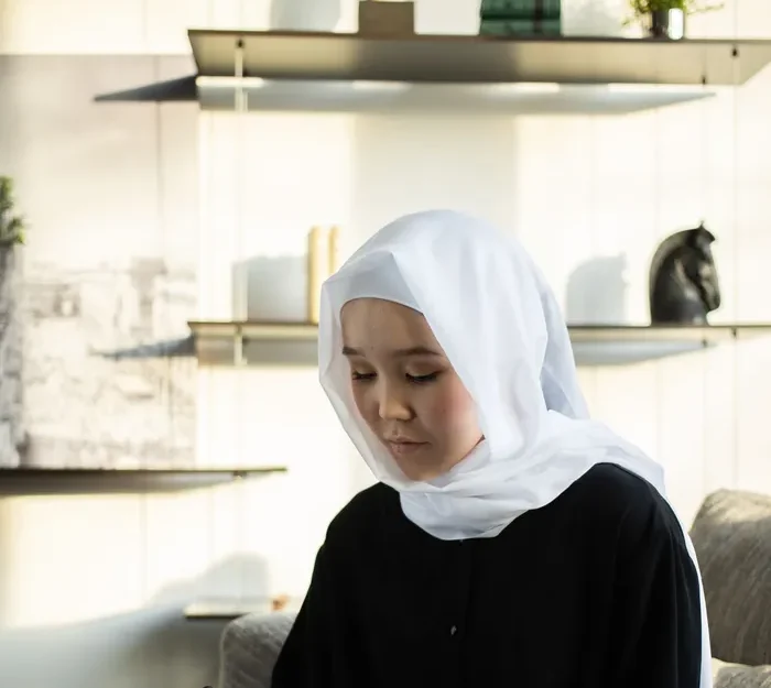 A female Quran teacher in a white hijab writing notes at a desk