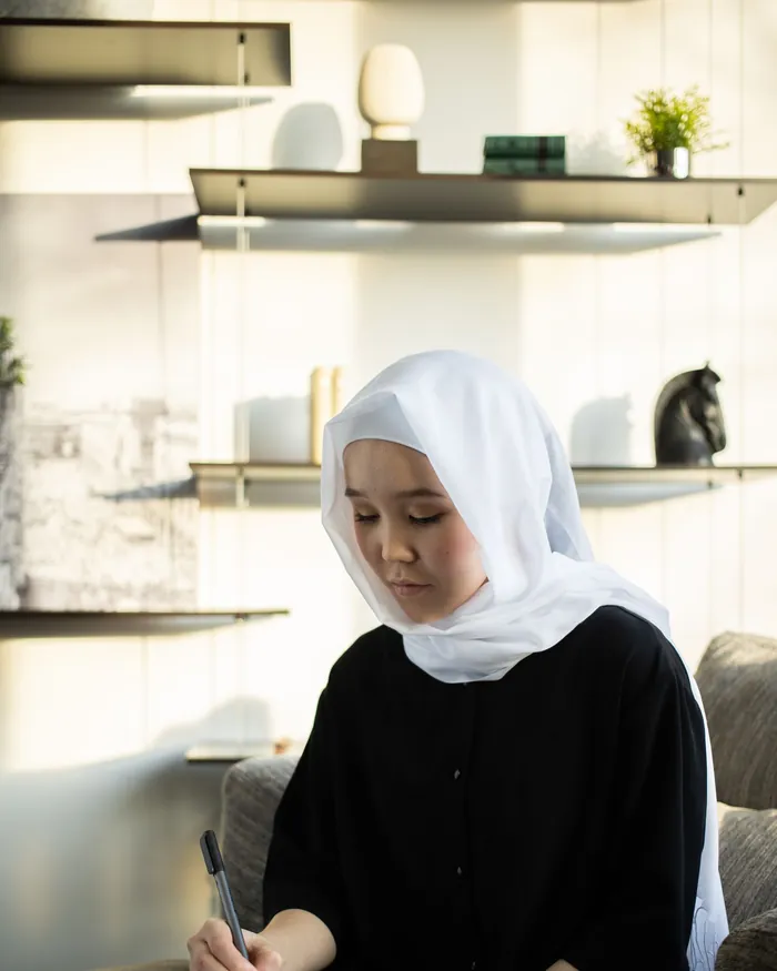 A female Quran teacher in a white hijab writing notes at a desk