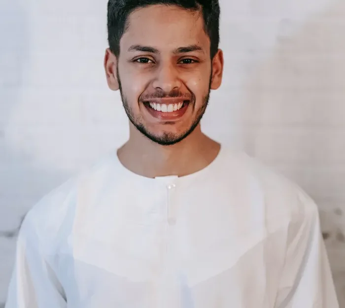 A male Quran teacher in a white thobe, photographed against a plain background