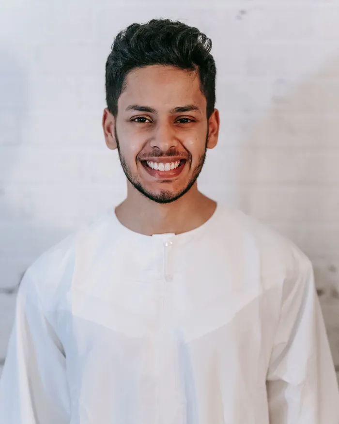 A male Quran teacher in a white thobe, photographed against a plain background