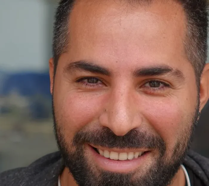 A smiling male Quran teacher with a beard, photographed in natural light