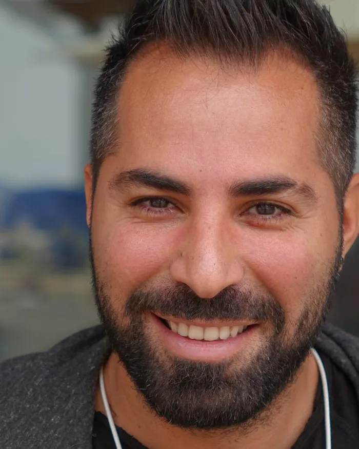 A smiling male Quran teacher with a beard, photographed in natural light