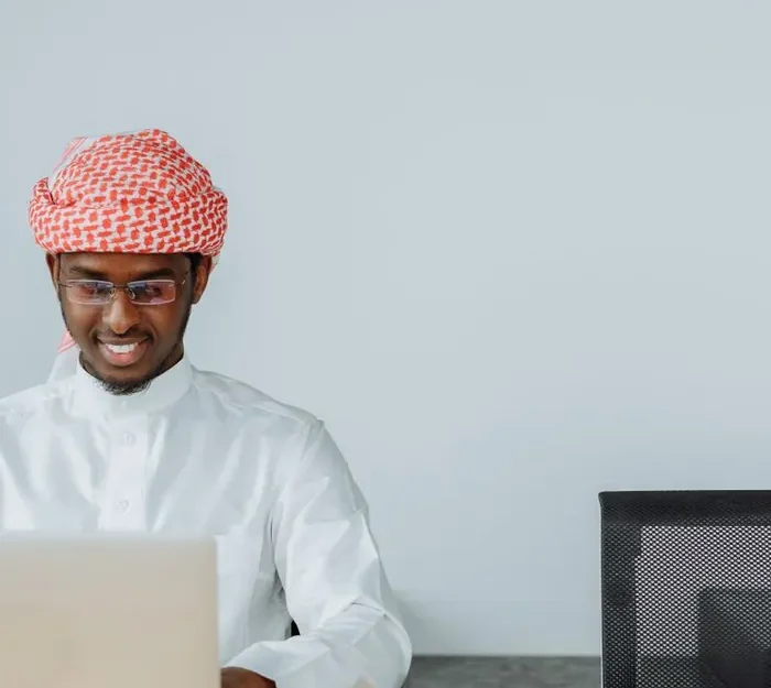 A male Quran teacher working at a laptop in a bright study