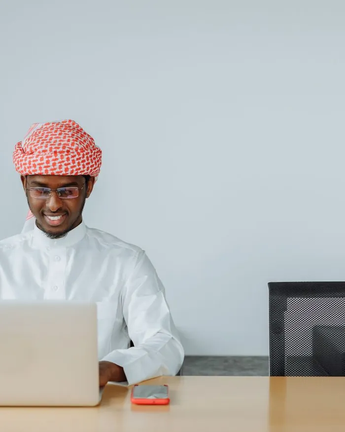 A male Quran teacher working at a laptop in a bright study